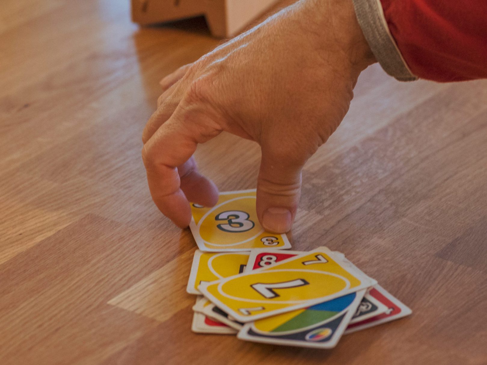Eine Person greift nach Uno-Spielkarten, die auf einem Tisch verteilt liegen.
