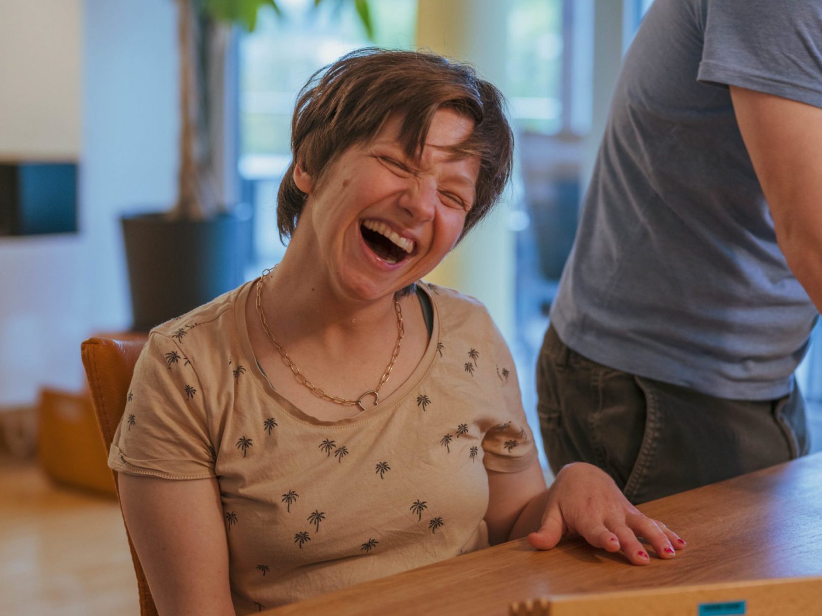 Eine Bewohnerin des Wohnhauses Brühlberg sitzt an einem Tisch und lacht.