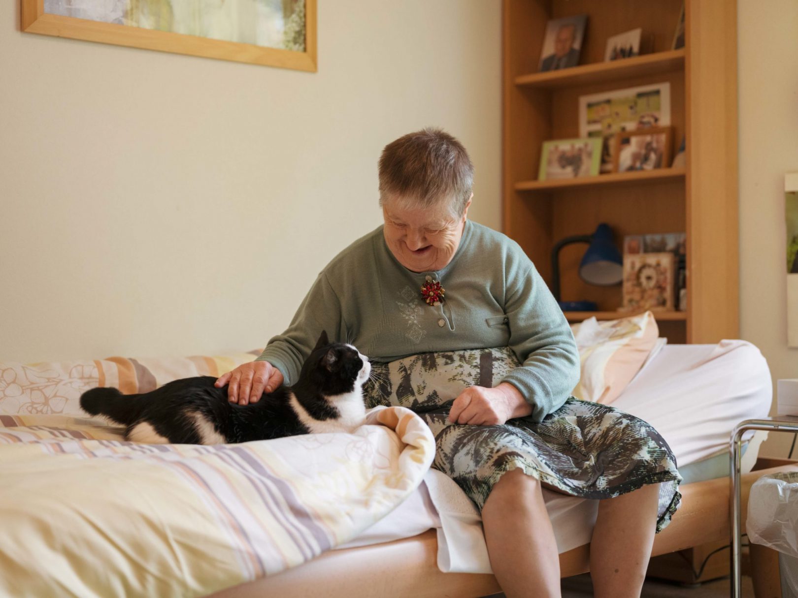 Eine Frau sitzt auf einem Bett und streichelt eine schwarz-weisse Katze.