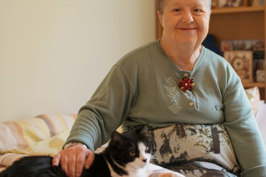 Eine Frau sitzt auf einem Bett und streichelt eine Katze.