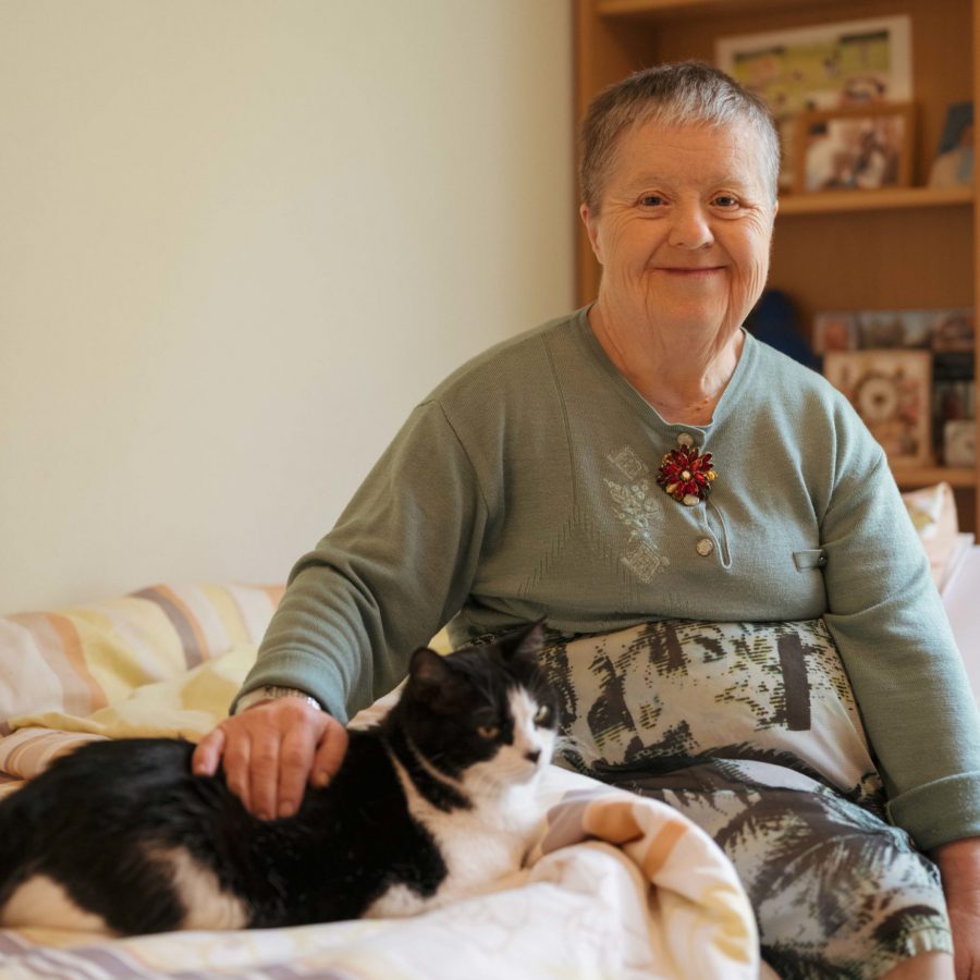 Eine Frau sitzt auf einem Bett und streichelt eine Katze.