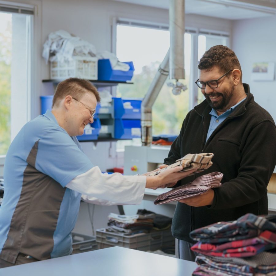 Zwei Personen in der Wäscherei stapeln zusammengefaltete Hemden.