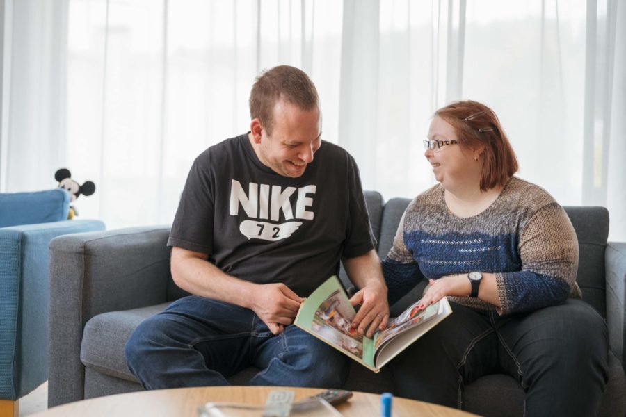 Ein Bewohner und eine Bewohnerin sitzen auf dem Sofa und schauen sich ein Buch an.