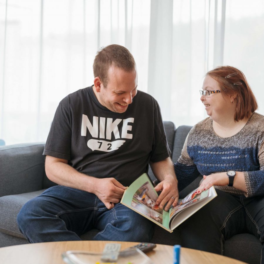 Ein Bewohner und eine Bewohnerin sitzen auf dem Sofa und schauen sich ein Buch an.