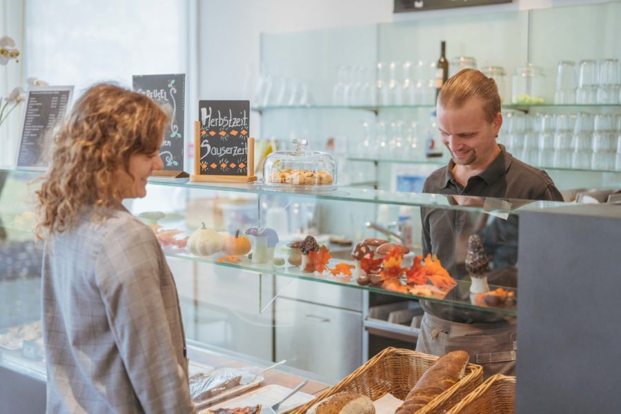 Eine lächelnde Frau steht vor der Bäckerei-Theke und bestellt etwas.