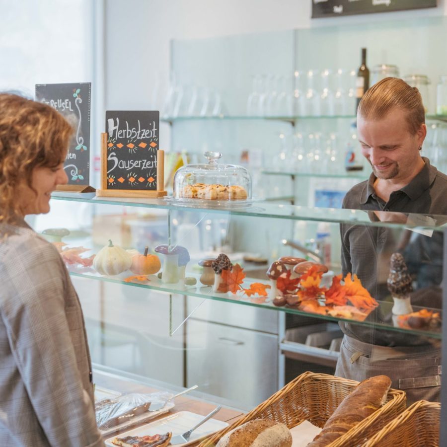 Eine lächelnde Frau steht vor der Bäckerei-Theke und bestellt etwas.