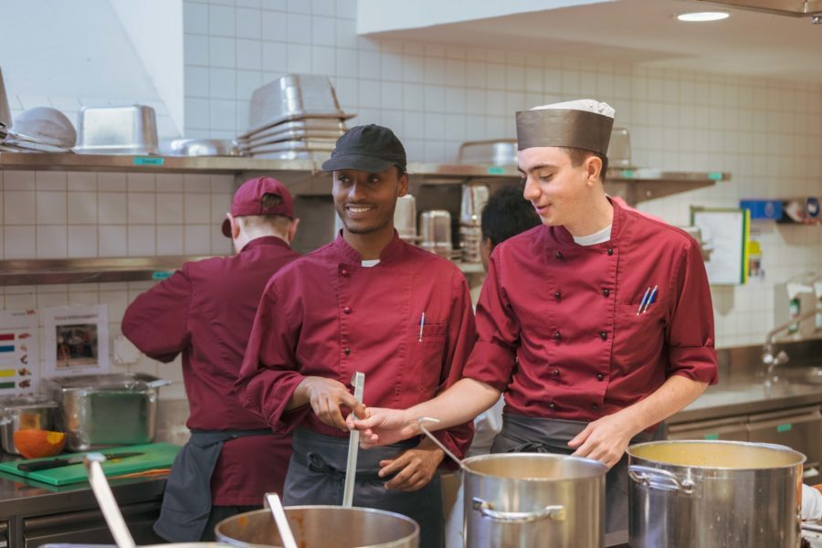 Drei Lernende der Brühlgut Stiftung stehen in der Küche des Restaurants Neumarkt am Herd und kochen.