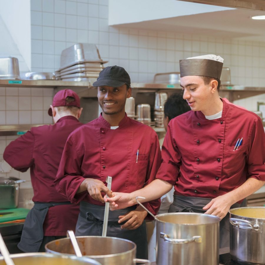 Drei Lernende der Brühlgut Stiftung stehen in der Küche des Restaurants Neumarkt am Herd und kochen.