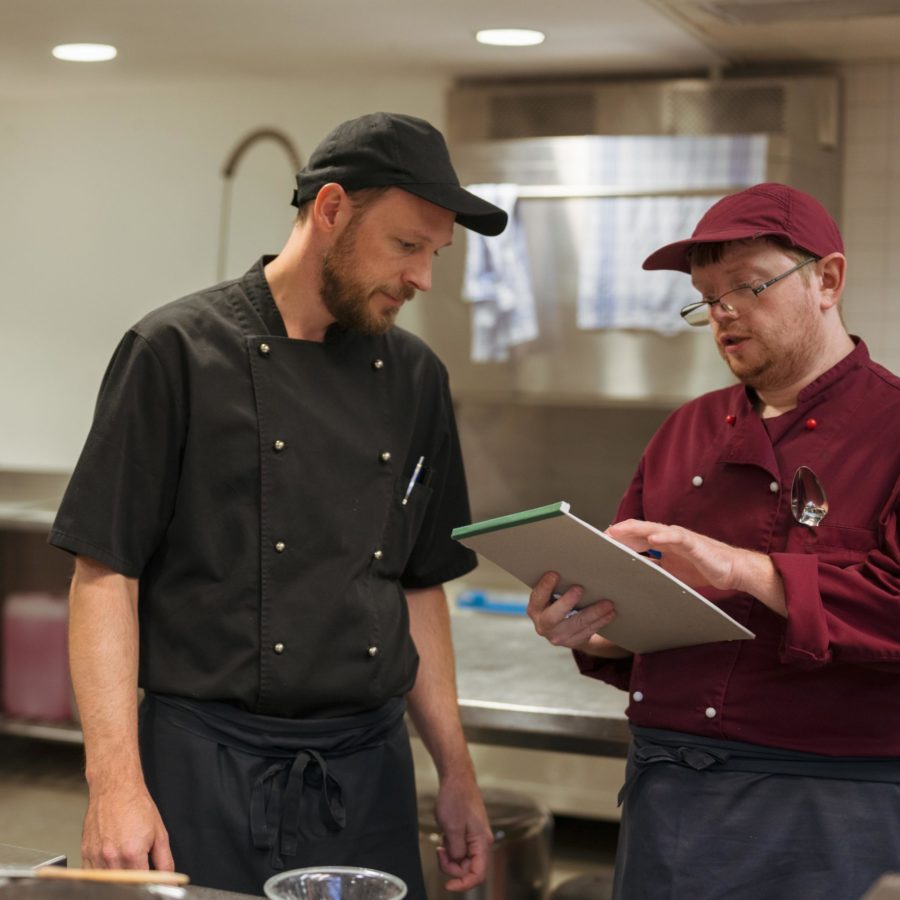 Ein Angestellter und ein Zivildienst der Brühlgut Stiftung studieren eine Liste in der Küche des Restaurants Neumarkt.