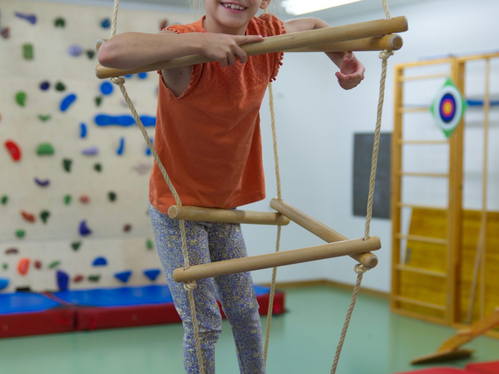 Ein Mädchen klettert auf einem hängenden Klettergerüst in der Physiotherapie.