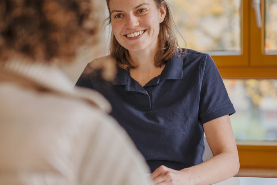 Eine Frau sitzt an einem Tisch und spricht mit einer anderen Frau.