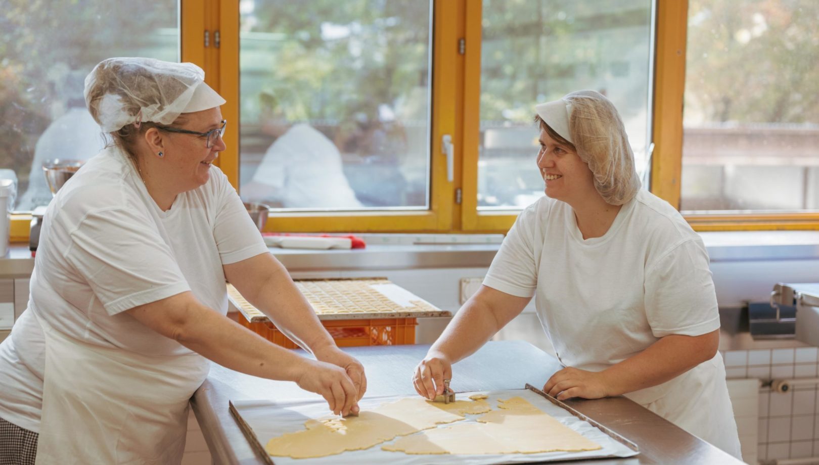 Zwei Frauen stehen mit Bäcker Hüten in der Brühlgut Bäckerei und stechen Kekse aus.