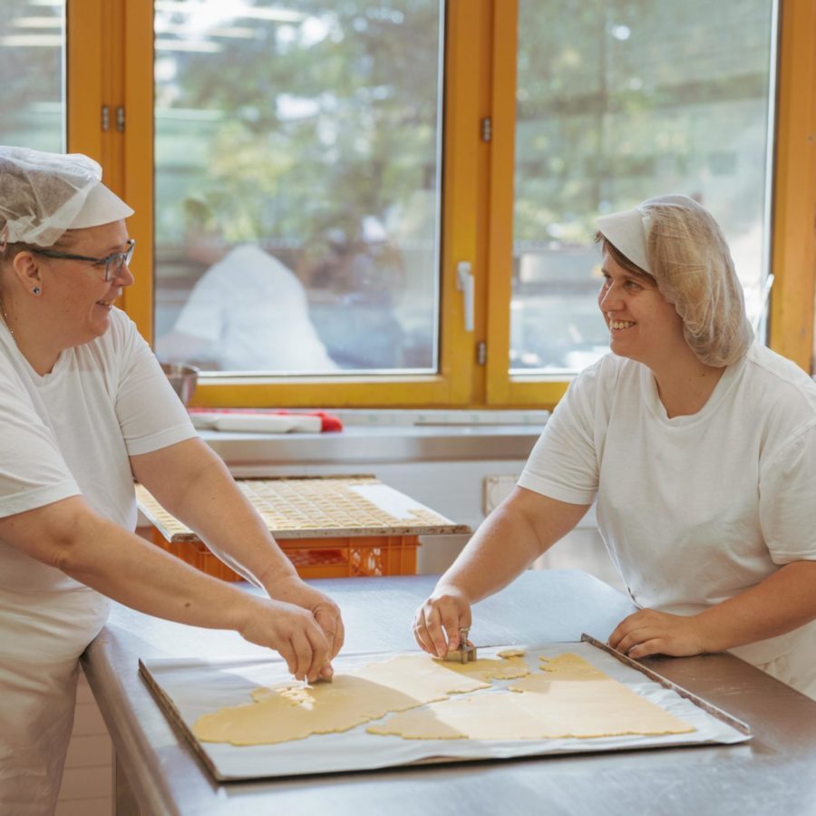 Zwei Frauen stehen mit Bäcker Hüten in der Brühlgut Bäckerei und stechen Kekse aus.