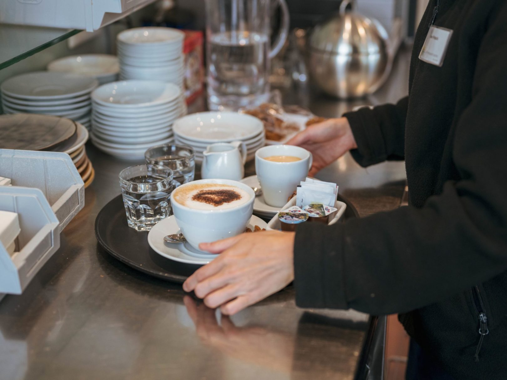 Eine Frau mit einem vollen Tablett mit Kaffee und Wassergläsern im Café Wyden.