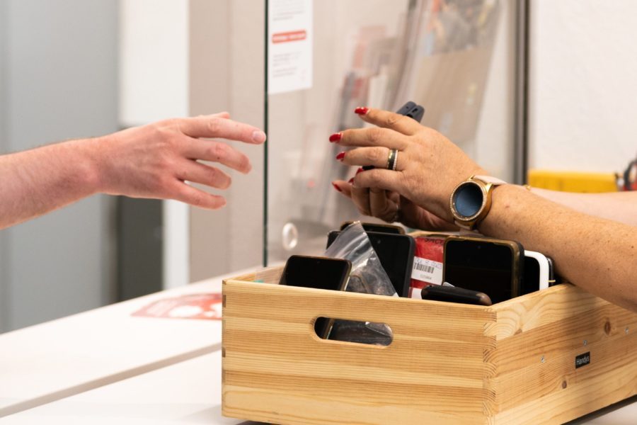 Eine Frau sitzt im Fundbüro und gibt jemandem einen verlorenen Gegenstand zurück.