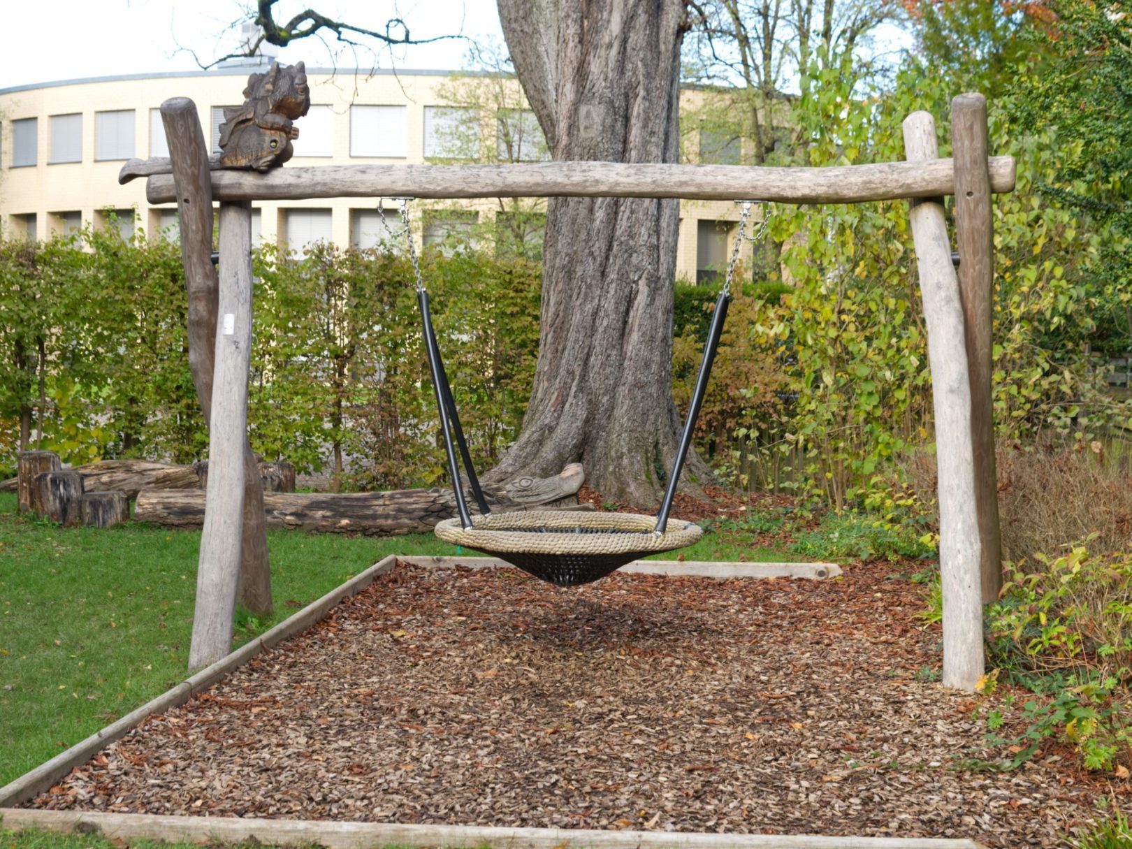Eine runde Holzschaukel vor der Kita Spielpark.