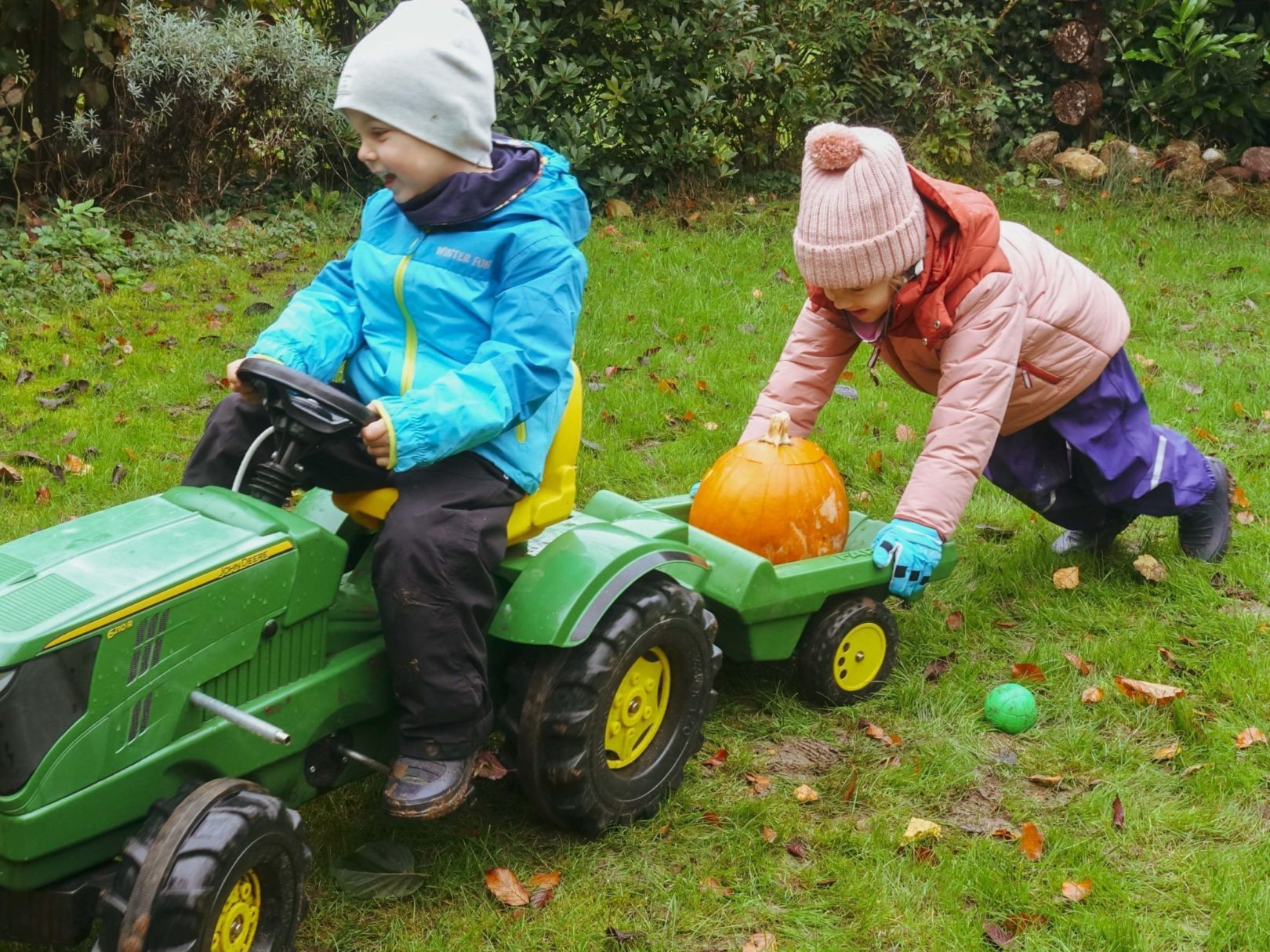 Zwei Kinder schieben einen Spielzeugtraktor auf dem Gras vor der Kita Spielberg.