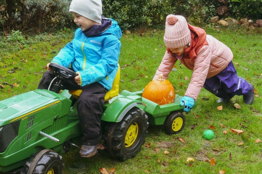 Zwei Kinder schieben einen Spielzeugtraktor auf dem Gras vor der Kita Spielberg.