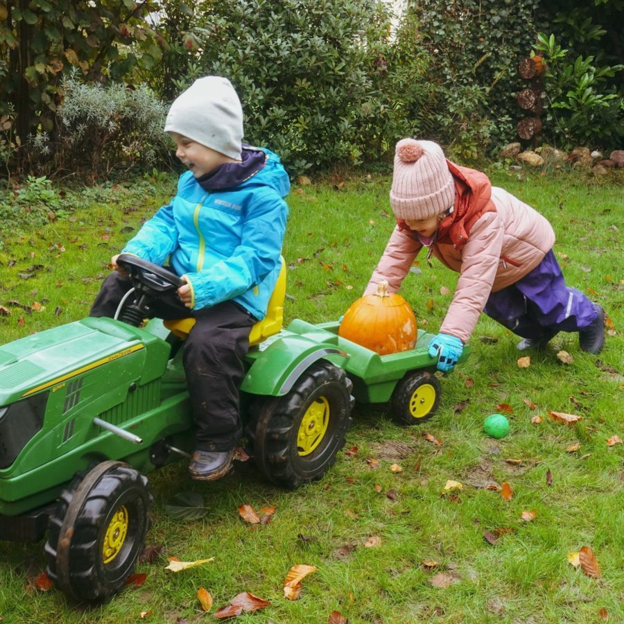 Zwei Kinder schieben einen Spielzeugtraktor auf dem Gras vor der Kita Spielberg.