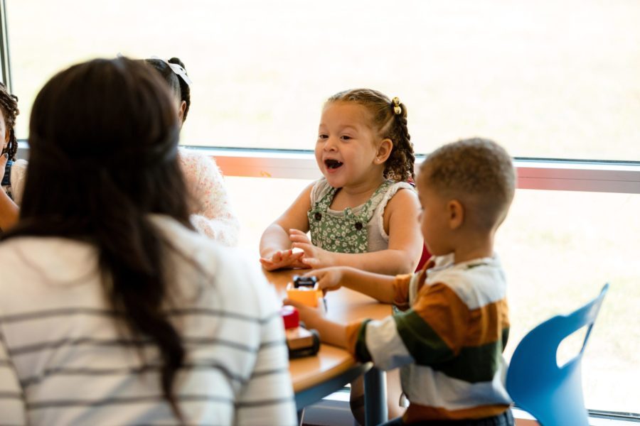 Mehrere Kinder sitzen in der Kita Spielblock mit einer Erzieherin an einem Tisch und spielen.