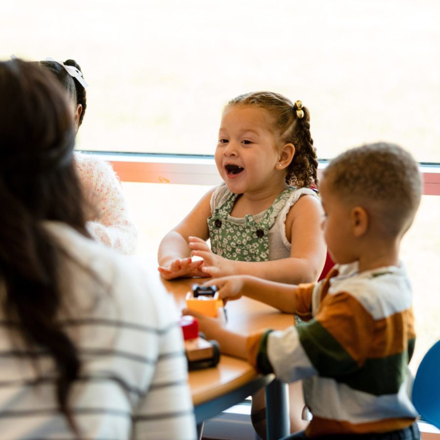 Mehrere Kinder sitzen in der Kita Spielblock mit einer Erzieherin an einem Tisch und spielen.