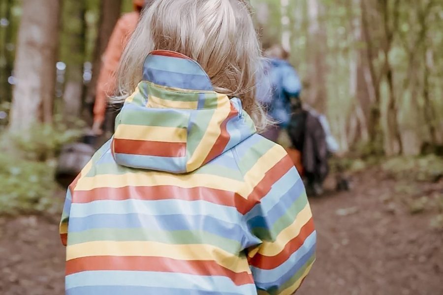 Ein Kind in einem farbigen Regenmantel geht durch den Wald.