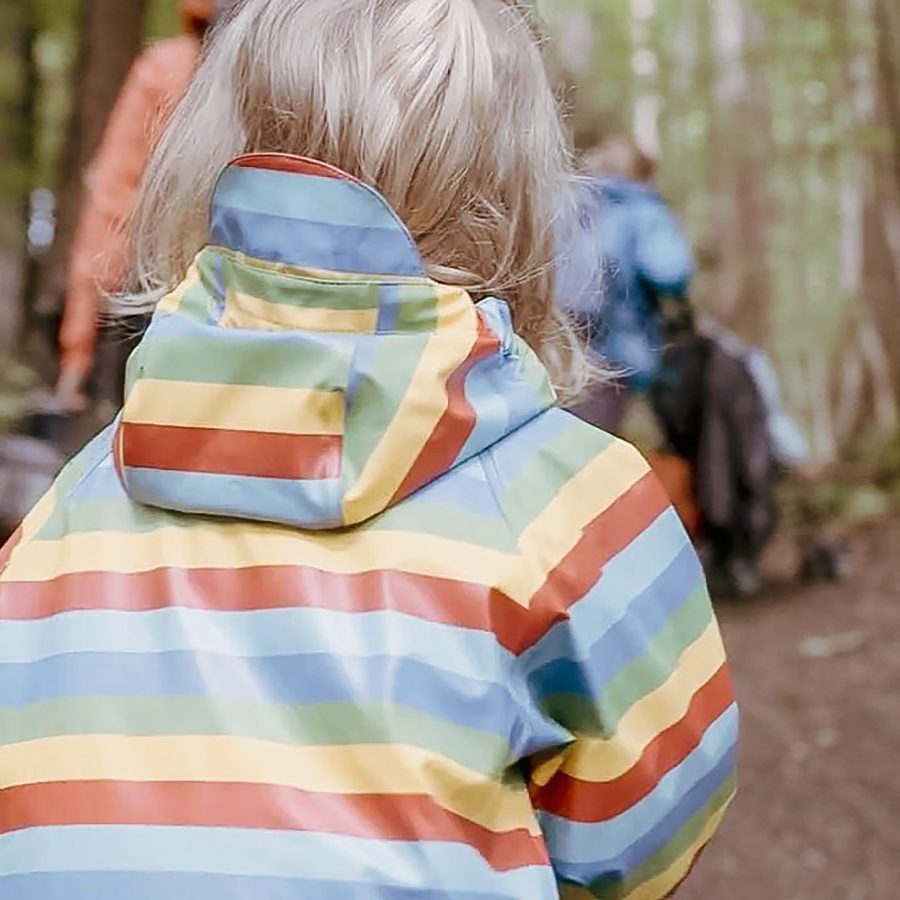 Ein Kind in einem farbigen Regenmantel geht durch den Wald.