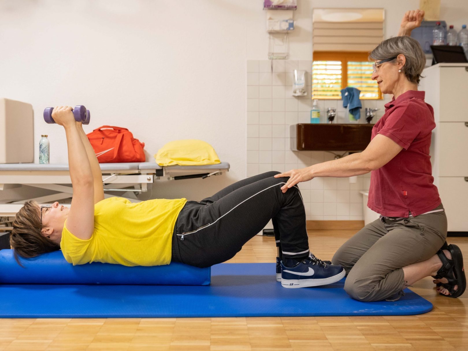 Eine Person liegt auf einer Matte und und wird von einer Physiotherapeutin an den Knien gestützt.