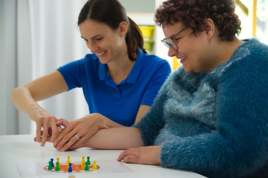 Eine Ergotherapeutin sitzt mit einer Bewohnerin am Tisch und bewegt ihre Hände.