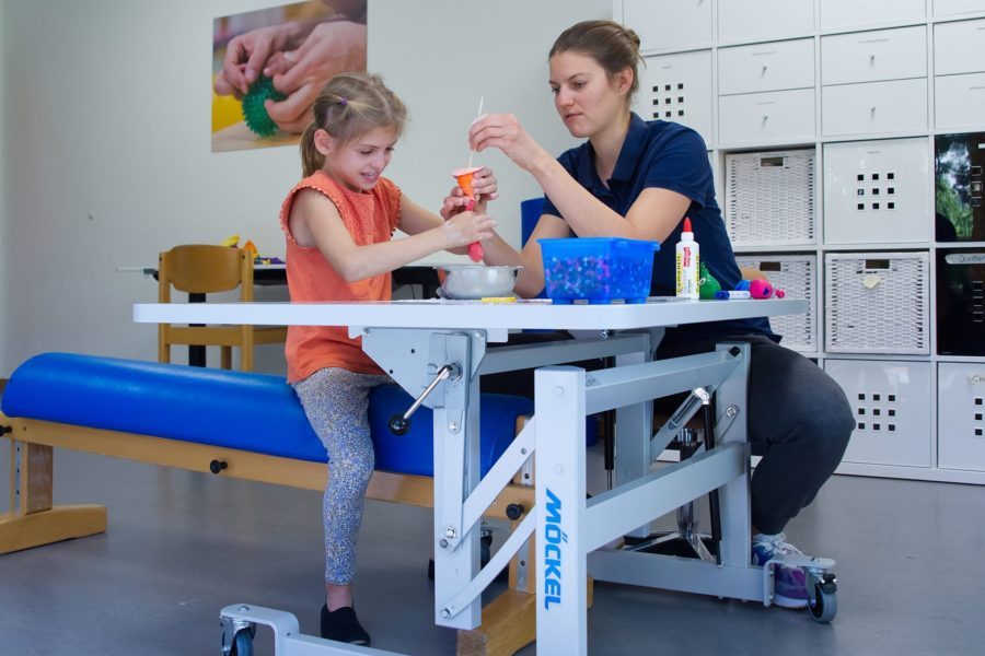 Eine Ergotherapeutin und ein Mädchen sitzen in einem Therapiezimmer und basteln.