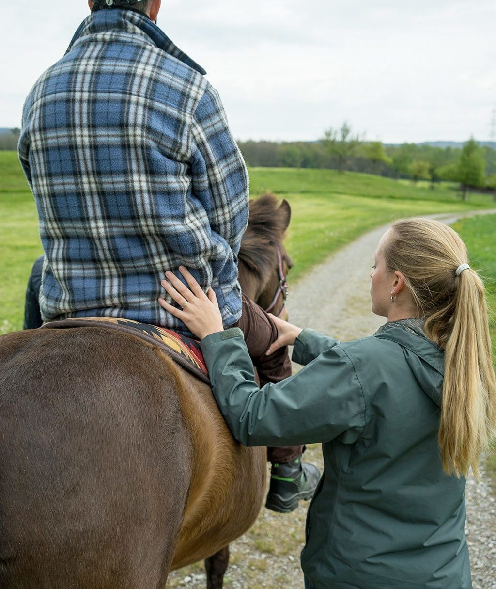 Ein Mann mit Helm auf einem Pferd während der Hippotherapie.