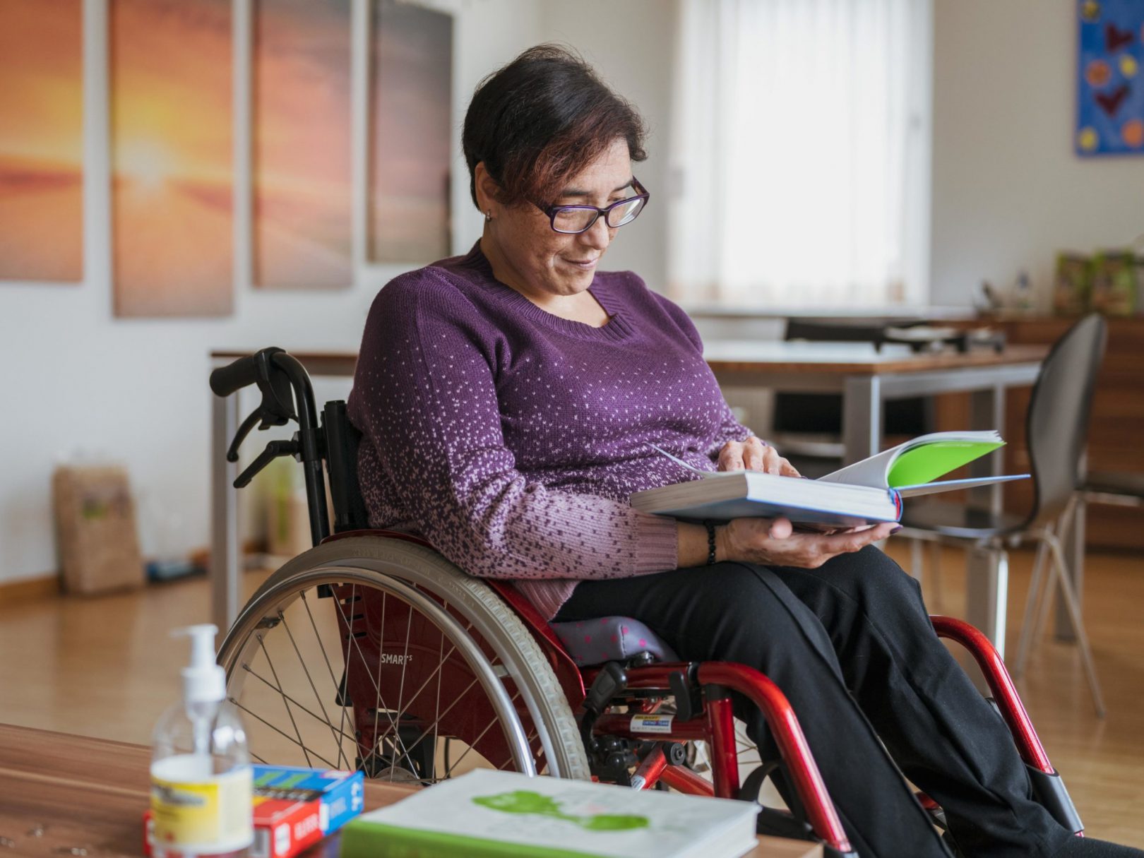 Eine Frau der Aussenwohngruppe sitzt im Rollstuhl und schaut ein Buch an.