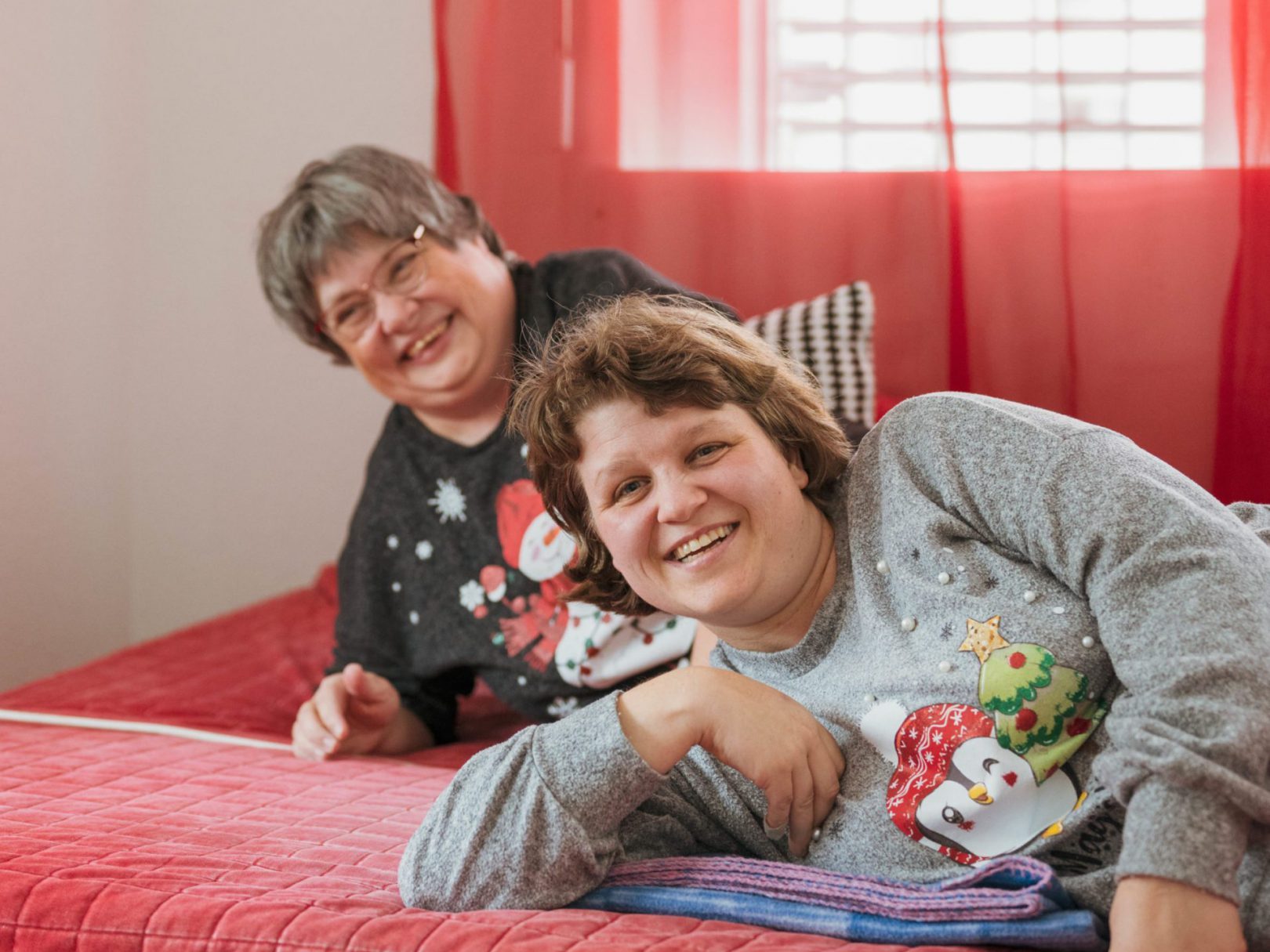 Zwei Bewohnerinnen der Aussenwohngruppe liegen auf einem Bett und lachen.