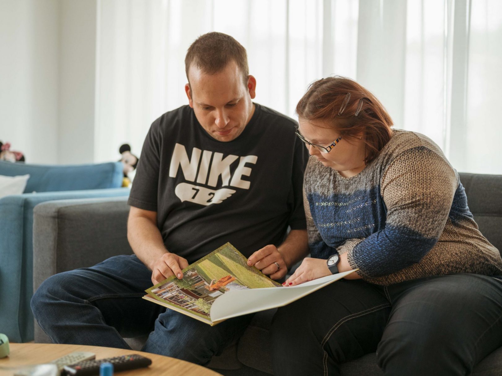 Ein Bewohner und eine Bewohnerin sitzen auf einem Sofa und schauen gemeinsam ein Buch an.