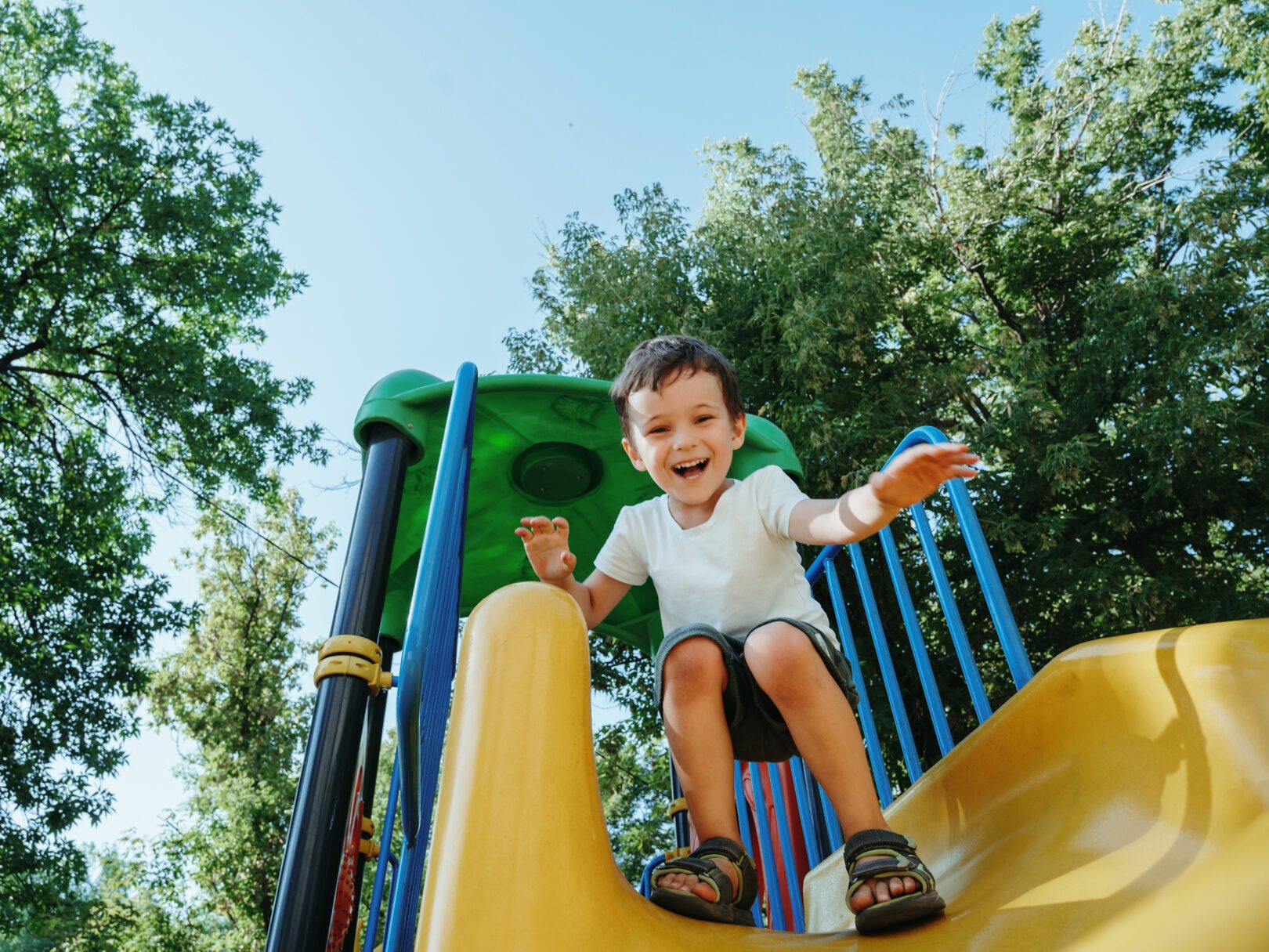 Glückliches Kita-Kind auf einer Rutsche auf dem Spielplatz im Sommer