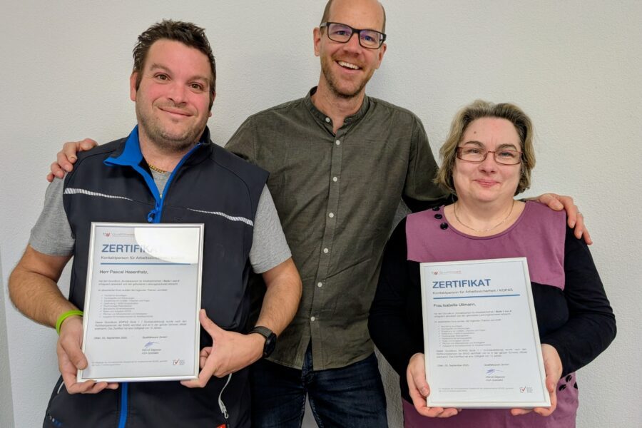 Eine Frau und ein Mann halten ein Zertifikat, ein weiterer Mann hat Freude.
