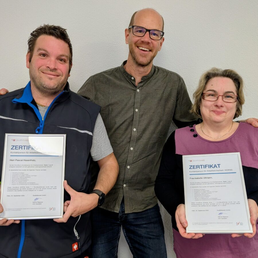 Eine Frau und ein Mann halten ein Zertifikat, ein weiterer Mann hat Freude.