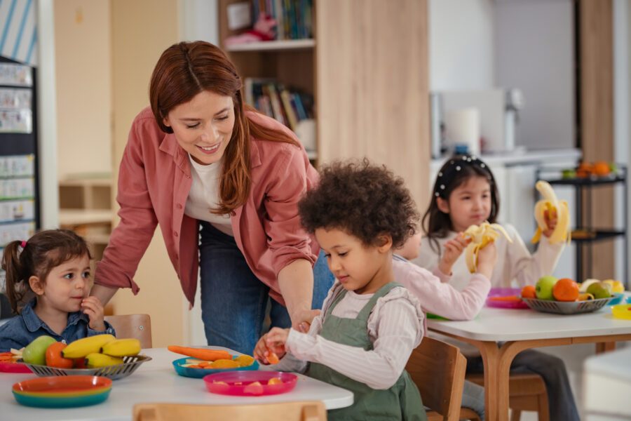 Kita Mitarbeiterin hilft Kindern Obst zu schneiden